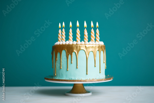 Elegant turquoise birthday cake with gold drip icing and gold birthday candles against a turquoise background photo