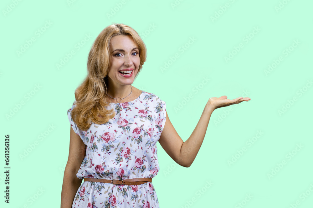 Mature caucasian woman presenting copy space with her left hand. Isolated on turquoise. Mature caucasian woman presenting copy space with her left hand. Isolated on turquoise.