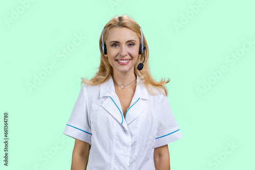 Portrait of happy blonde doctor wearing headset. Isolated on turquoise.