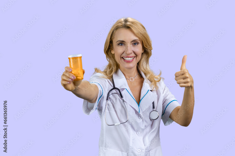 Portrait of happy caucasian female doctor holding a can of pills and gives her thumb up. Isolated on purple. Portrait of happy caucasian female doctor holding a can of pills and gives her thumb up. Isolated on purple.