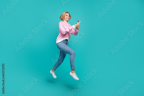 Full length photo of funky positive lady wear pink pullover chatting modern device jumping empty space isolated turquoise color background