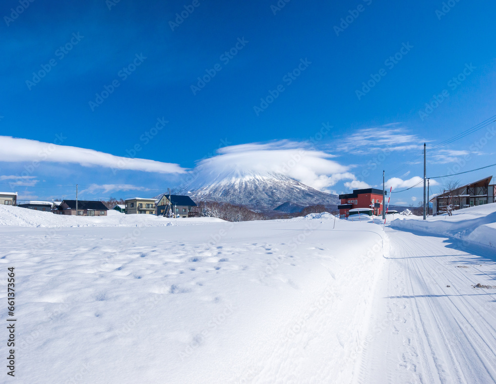 View of snowy volcano with a cap cloud beyond snowfields in a heavy snowfall town (Niseko, Hokkaido, Japan)