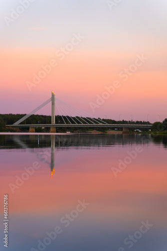 Vertical photo. An Lovely sunset in Rovaniemi Finland. Polar day. Traveling to Lapland. Pink sky over the bridge. Vacation in the north. Reflection in the water. Color gradient. Fantastic Scandinavia
