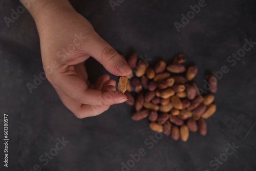 Female hand showing a roasted peanut over dark background. Healthy food.