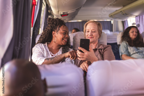 Jovem ensinando mulher idosa a usar o aplicativo de transporte urbano em seu smartphone, durante viagem de onibus. photo