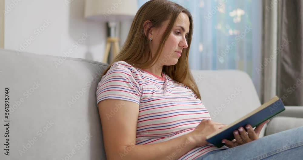 Young pretty woman reading book while resting on comfortable sofa at home Young pretty woman reading book while resting on comfortable sofa at home