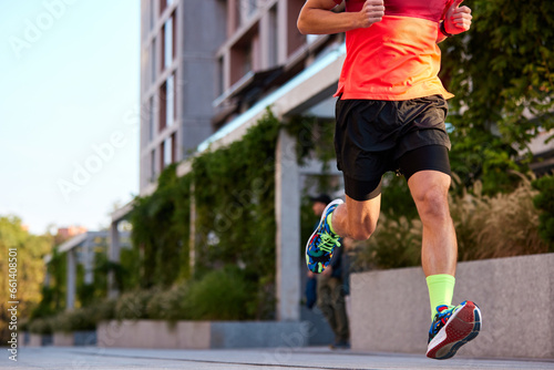 Cropped image of athletic man in sportswear and running shoes training, running outdoors on early summer morning. Concept of sport, active and healthy lifestyle, competition, dynamics, marathon