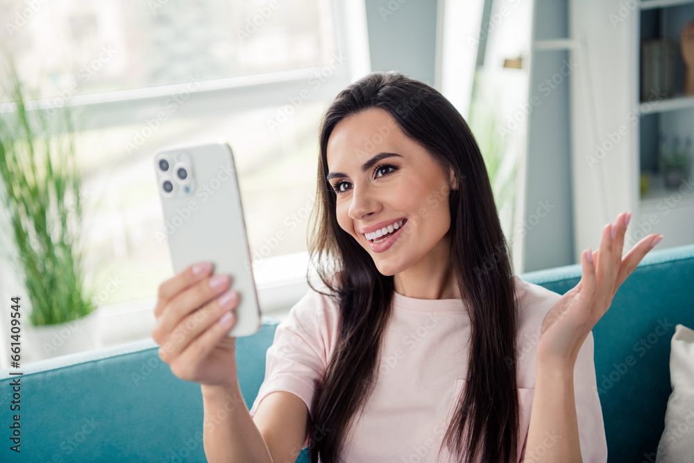 Photo of pretty positive lady sit couch hold smart phone blogging communicate video call house indoors