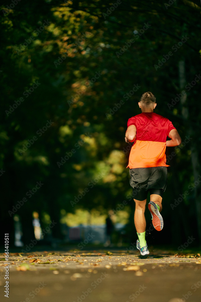Sunny morning outdoor training. Back view. Muscular, athletic man in sportswear, runner in motion, running in city park. Concept of sport, active and healthy lifestyle, competition, dynamics, marathon