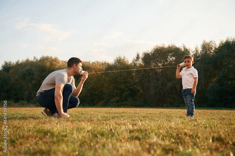 Talking by using string can phone. Father and little son are playing and having fun outdoors