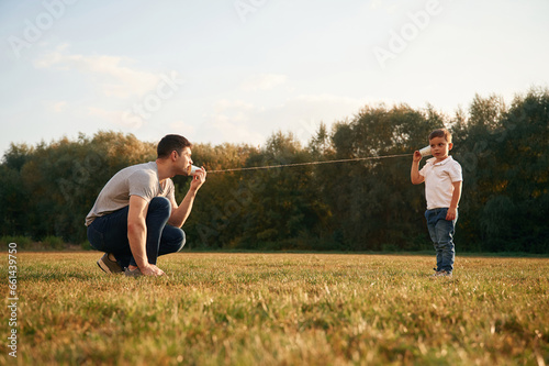 Talking by using string can phone. Father and little son are playing and having fun outdoors