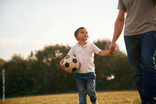 Walking and holding soccer ball. Father and little son are playing and having fun outdoors © standret