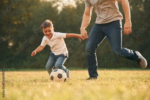 View of the field, with soccer ball. Father and little son are playing and having fun outdoors