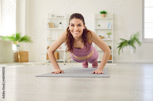 Portrait of a young attractive sporty woman doing push-up or plank sport exercises lying on yoga mat on the floor in the living room at home. Fitness, workout and home training concept.