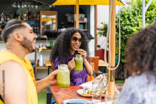 Gay man and afro woman smiling and enjoying a delicious meal on the terrace of an outdoor restaurant.