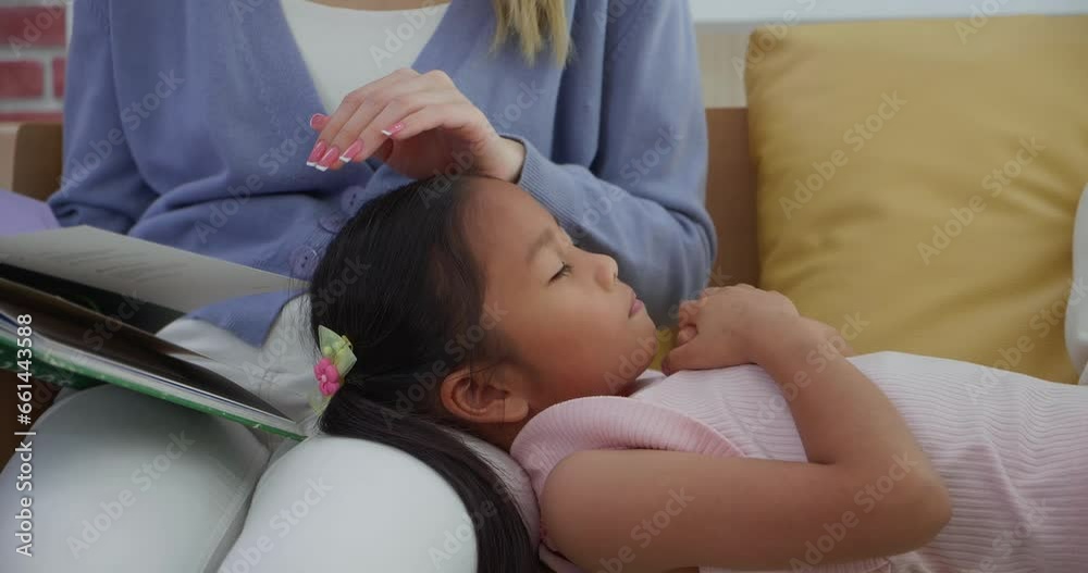 Asian little girl sleeping on mother's lap while listening story book or fairy tales from mother in living room at home. Family relationships concept