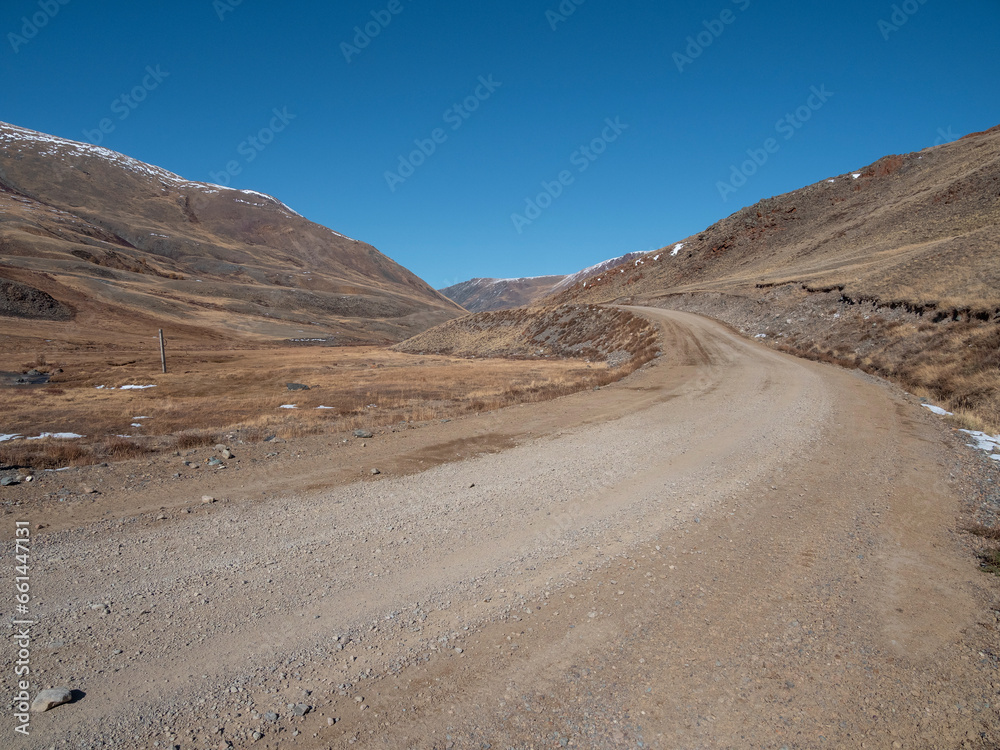 Dirt road uphill. Dangerous narrow dirt mountain road through the hills to a high-altitude village. Altai region. Dirt road uphill. Dangerous narrow dirt mountain road through the hills to a high-altitude village. Altai region.