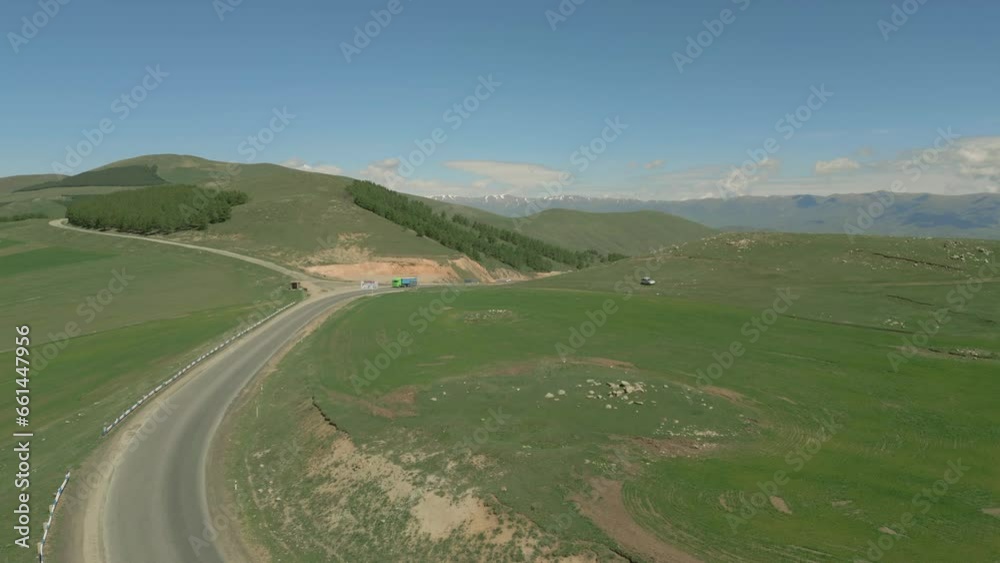 Drone Video. Flying forward along the highway, on which cars drive, between green grassy hills on a sunny day. Against a backdrop of high snowy mountains. Lori, Armenia. Drone Video. Flying forward along the highway, on which cars drive, between green grassy hills on a sunny day. Against a backdrop of high snowy mountains. Lori, Armenia.