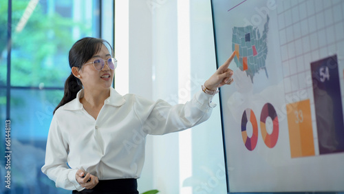 young asian business woman standing in front of television screen giving presentation and Explaining Graphs in office . speaker with whiteboard presenting  idea to colleagues in meeting