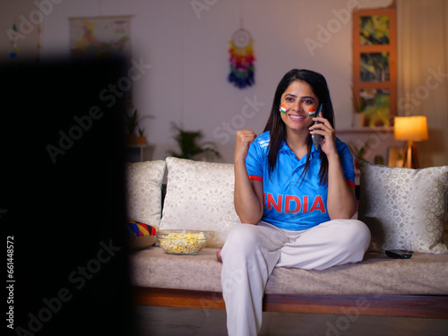 Young Indian woman celebrating Indian cricket team's victory - watching live cricket sports match on TV.. Female Indian cricket fan wearing an Indian jersey - excitement  cheering for team  female ...