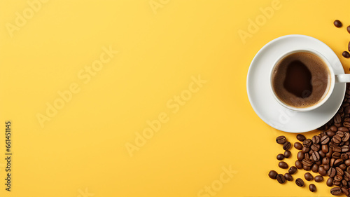 A steaming cup of coffee on a saucer with scattered roasted coffee beans on a vibrant yellow background photo
