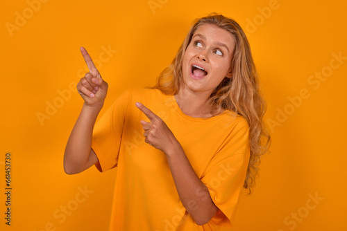 Canvas Print Young shocked expressive Caucasian woman teen points to side and opens mouth feeling fear and trepidation from unexpected advertising or large discounts stands posing on yellow background