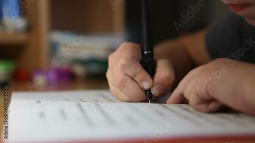 A boy, a 3rd grade student, writes his homework in a notebook. The child does his homework at home.
