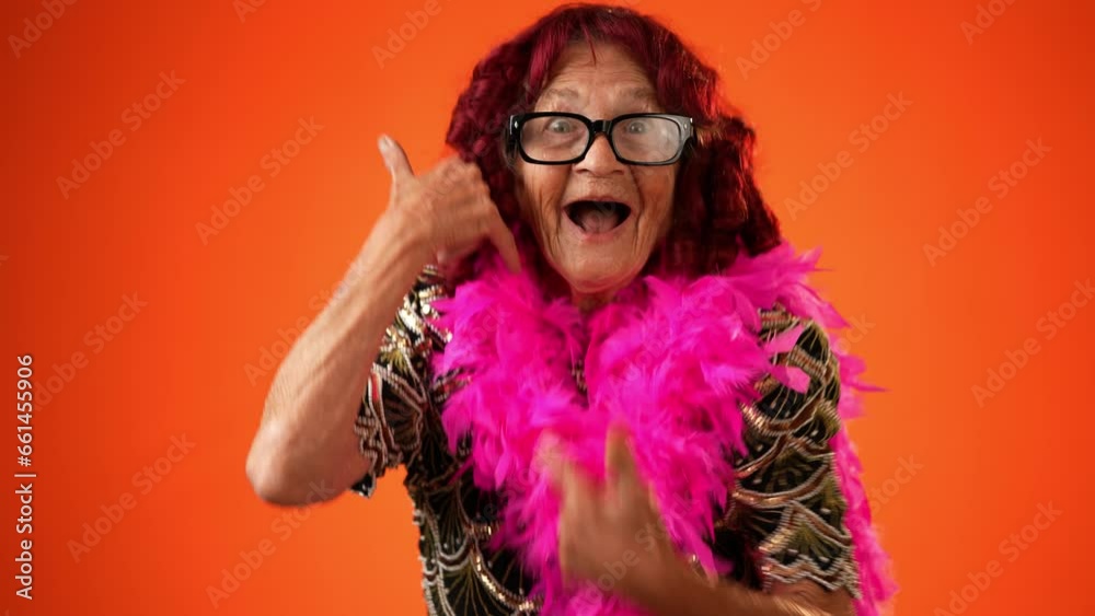 Funny portrait of smiling happy elderly senior old woman with wrinkled skin smiling pointing to camera and giving call me gesture with hands isolated on solid orange background. Funny portrait of smiling happy elderly senior old woman with wrinkled skin smiling pointing to camera and giving call me gesture with hands isolated on solid orange background.
