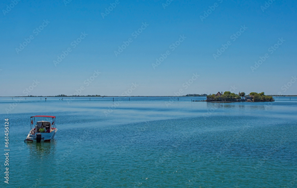 A speed boat in the Grado section of the Marano and Grado Lagoon in Friuli-Venezia Giulia, north east Italy. A traditional casone fisherman's hut is seen on an island in the background. August