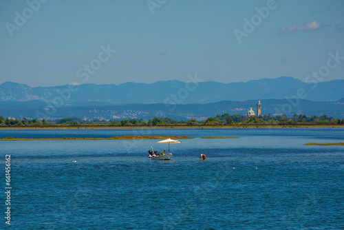 Fishing for cockles from a speed boat in the Grado section of the Marano and Grado Lagoon in Friuli-Venezia Giulia, north east Italy. The Santuario di Barbana Church is seen in the background. August © dragoncello