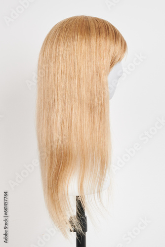 Natural looking blonde wig on white mannequin head. Long hair on the plastic wig holder isolated on white background  side view.