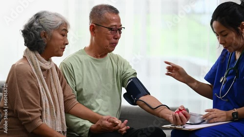 Female healthcare worker measuring arterial blood pressure elderly male during home visit. Elderly healthcare and hypertension concept photo