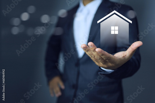 Businessman holding home icon in hand to present an advantage of construction project to customers and provide best facility management to residense area with technology and iot modern house.
