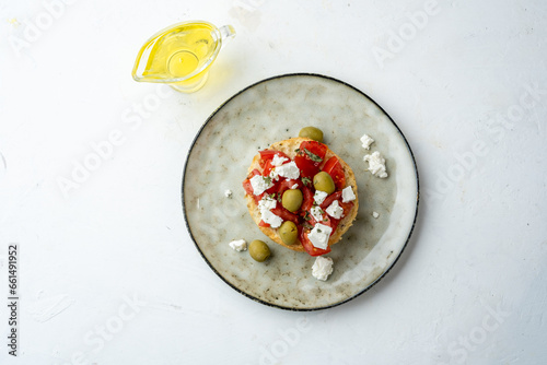 Dakos is a delicious Greek appetizer made with tomatoes, olive oil and fresh tomatoes. Top view, light table.