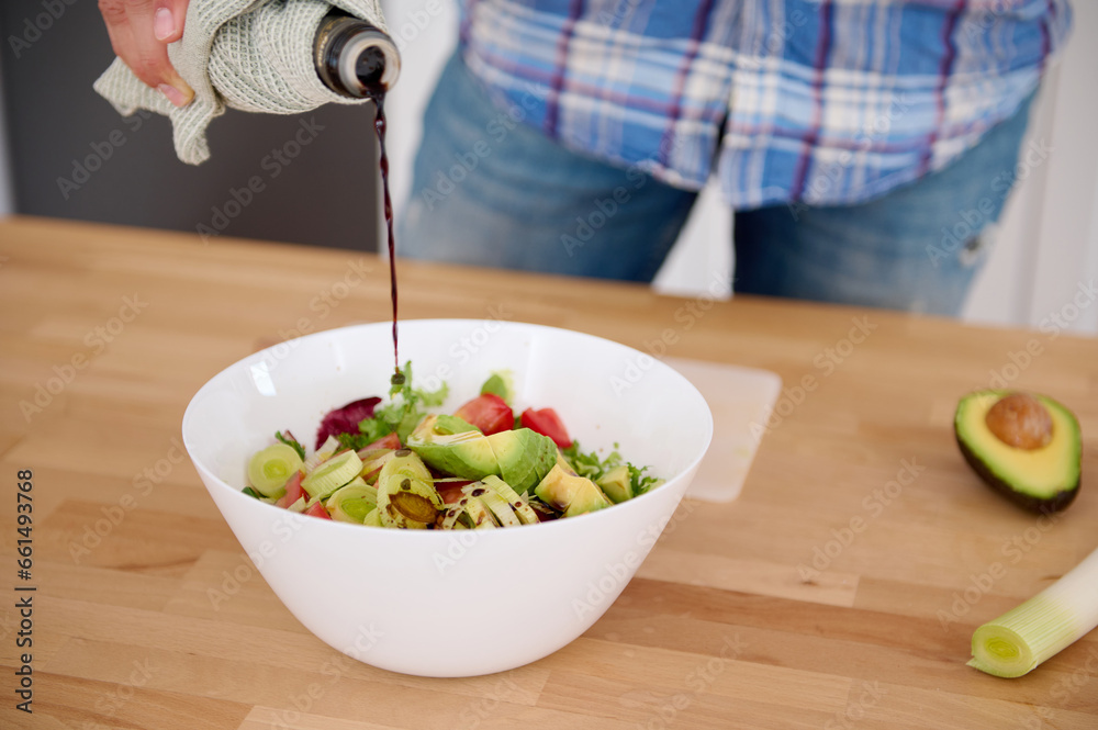 Detail on the hands of chef pouring balsamic vinegar into a bowl of fresh salad while cooking in minimalist home kitchen Detail on the hands of chef pouring balsamic vinegar into a bowl of fresh salad while cooking in minimalist home kitchen