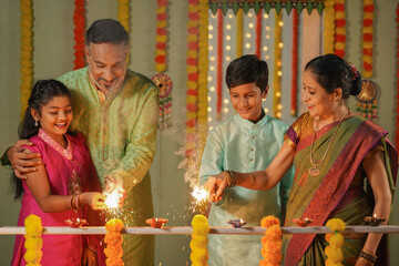 Happy Grandparents playing with sparklers or Crackers with Kids near balcony at home during diwali festival celebration - concept of Traditional culture, Familt generation and Caring family