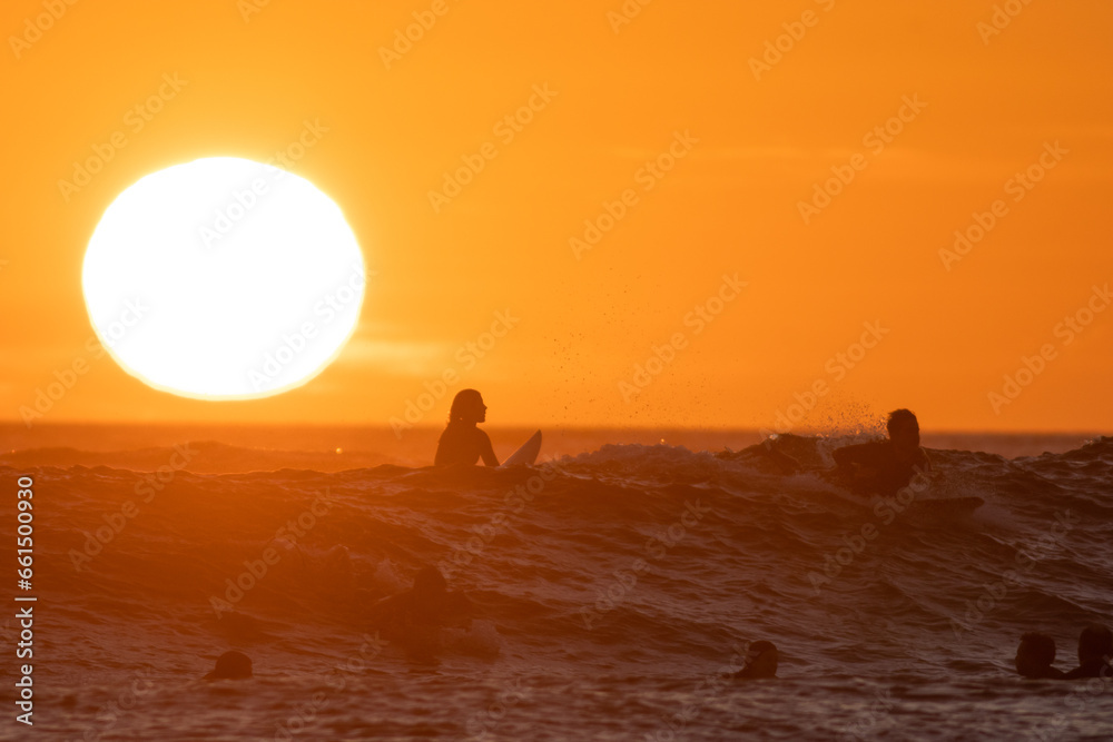 Surfers swimming in the sea at bright orange sunset - huge shining sun