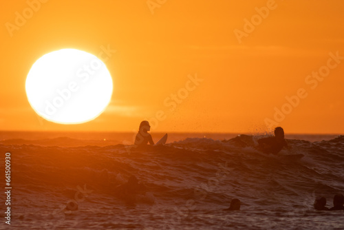 Surfers swimming in the sea at bright orange sunset - huge shining sun