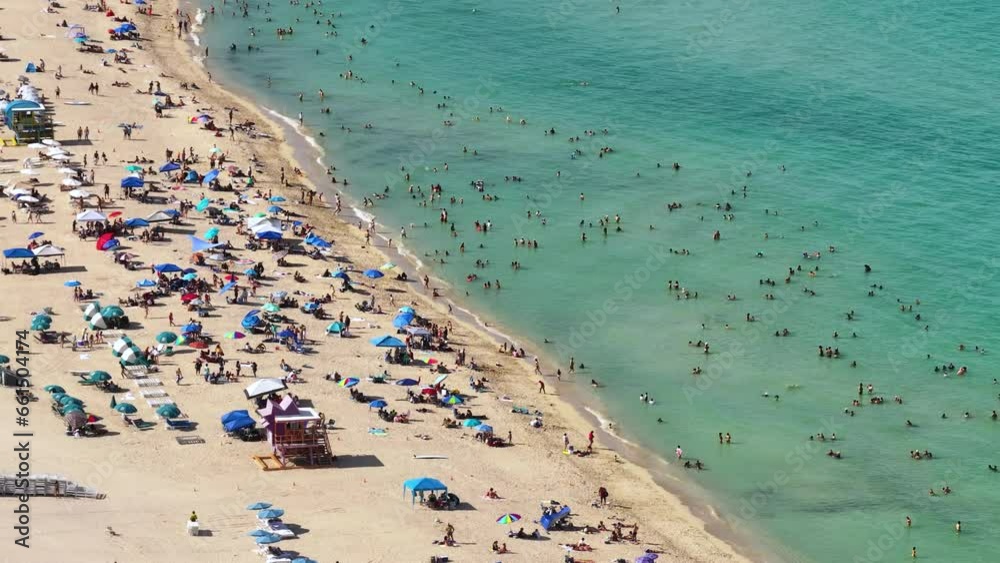 Crowded South beach in Miami, USA. Many people enjoying vacations time swimming in ocean water and relaxing on warm Florida sun Crowded South beach in Miami, USA. Many people enjoying vacations time swimming in ocean water and relaxing on warm Florida sun
