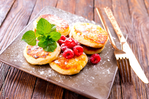 Traditional sweet syrniki or cottage cheese pancakes served with sweet cream and fresh raspberries in a white plate over table. photo