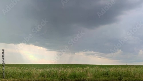 Pouring rain and wind on green field landscape with scenic heavy gray clouds, rural landscape
