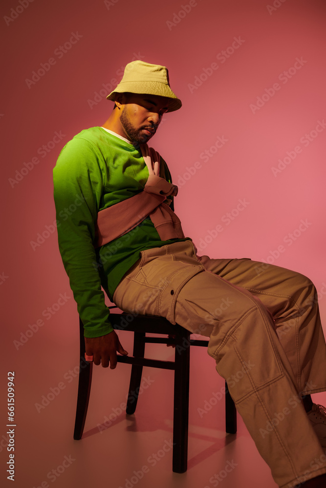 good looking african american man in green sweatshirt and panama sitting on chair, fashion concept
