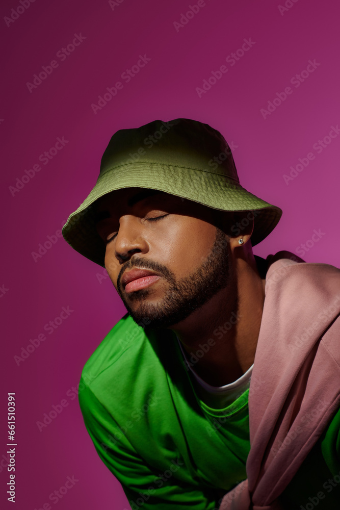 bearded african american man in green panama with closed eyes on purple backdrop, fashion concept