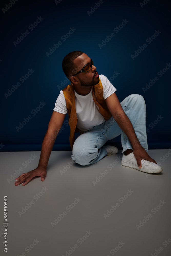trendy man in casual stylish outfit posing on floor looking away, hand to foot, fashion concept trendy man in casual stylish outfit posing on floor looking away, hand to foot, fashion concept