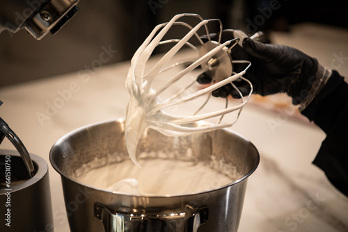 Hand holding a mixing whisk near the mixer bowl, preparing heavy cream and cheese. close up, front view.