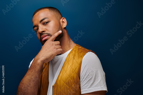 portrait of african american male model in trendy yellow vest, fingers on face, fashion concept