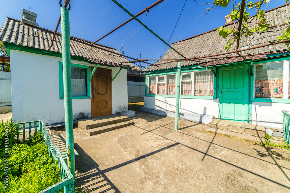 a dilapidated one-story rural house. Green lawn and trees. Whitewashed walls, green window frames. a dilapidated one-story rural house. Green lawn and trees. Whitewashed walls, green window frames.