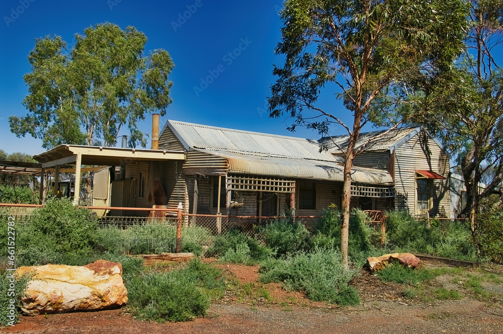 Abandoned cottage made of corrugated iron and wood, with an overgrown garden, in the former gold mining town of Kookynie, now a ghost town, shire of Menzies, Western Australia

