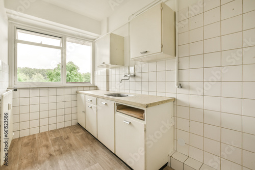 a kitchen with white tiles on the walls and wood flooring in front of the window looking out to the trees outside
