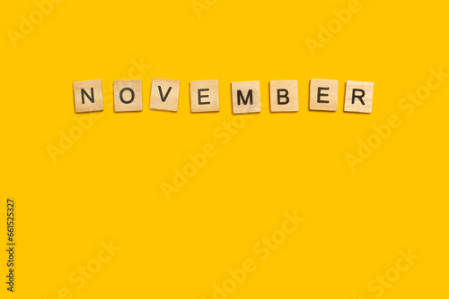 Bloques de madera formando la palabra November sobre un fondo amarillo liso y aislado. Vista superior. Copy space